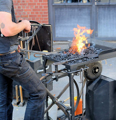 Familienfest beim Museum der Arbeit in Hamburg Barmbek Nord - Schmiede der Metallgruppe vom Museum der Arbeit führen ihre Kunst vor. Feuerstelle, Esse mit Flammen - ein Metallstab wird im Schmiedefeuer zum Glühen gebracht.