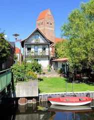 Wohngebäude am Wassergang an der Elde in Parchim - rotes Ruderboot am Ufer; Kirchturm der St. Marienkirche.