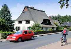 Reetgedecktes Wohnhaus mit weisser Putzfassade - fahrendes Auto, Fahrradfahrer; Kisdorfer Strasse in Henstedt / Henstedt-Ulzburg.