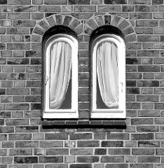 Schmale Fenster mit Gardinen / symmetrisch - Backsteinfassade in Hamburg Alsterdorf; schwarz - weiss Aufnahme.