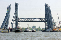 Drei Schlepper passieren die hochgefahrene Rethehubbrücke in Hamburg Wilhelmsburg und fahren vom Reiherstieg in die Rethe ein. Im Vordergrund Teile der Brückenkonstruktion für die neue Klappbrücke.