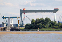 Blick über die Elbe zur Estemündung - Klappbrücke über die Strasse - 300 t Werftkran der Sietas Werft. Ein Spaziergänger auf dem Watt, das bei Niedrigwasser im Mühlenberger Loch entsteht.