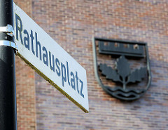 Schild Rathausplatz - Gemeindewappen von Henstedt-Ulzburg; dreiblättriger Echenzweig, Mauerkrone + Wellenfäden.