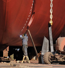 Ein Werftarbeiter schweisst an einem Schiffsrumpf - der Schiffsanker hängt an einer schweren Kette auf dem Boden des Docks einer Werft auf Hamburg STeinwerder.