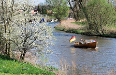 Blühende Bäume am Ufer der Este in Hamburg Cranz - ein Motorboot fährt auf dem Fluss.