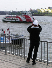 Blick von den St. Pauli Landungsbrücken auf die Elbe - eine Hafenfähre legt an. Zelt König der Löwen am anderen Elbufer.