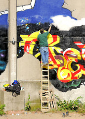 Sprayer bei der Arbeit auf einer Leiter - entstehen eines Grafittis an einer Gebäudewand in der Hafencity Hamburg.