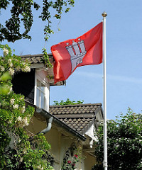 Eine Hamburg Fahne weht im Wind in einem Vorgarten von Blankenese.