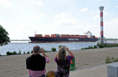 Containerschiff auf der Elbe - Elbstrand mit Leuchtturm von Hamburg Blankenese - ein Paar fotografiert das riesige Frachtschiff.