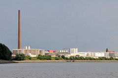 Tanklager und hoher Ziegelschornstein am Ufer des Reiherstiegs in Hamburg Wilhelmsburg.