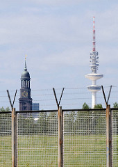 Zollzaun am Klütjenfelder Hauptdeich - hinter dem Stacheldraht der Hamburger Fernsehturm und der Kirchturm der St. Michaeliskirche.