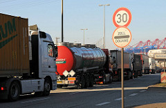 Warteschlage von Lastkraftwagen vor der Zollabfertigung beim Hauptzollamt Hamburg Waltershof. Verkehrschilder - Geschwindigkeitsbegrenzung auf 30 km/h und "Zoll - Douane". Im Hintergrund Contaienbrücken des Containerterminals EUROGATE.