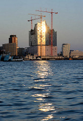 Abendsonne im Hamburger Hafen - die untergehende Sonne spiegelt sich in der Glasfassade der entstehenden Elbphilharmonie in der Hamburger Hafencity.