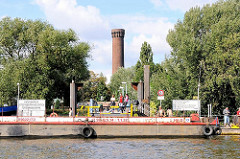 Anleger Entenwerder in Hamburg Rothenburgsort. Eine Schute hat am Ponton festgemacht, dahinter der Ziegelturm der Wasserspiele von Hamburg Rothenburgsort.