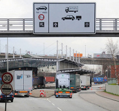 Einfahrt Zollstation Waltershof - Freihafengrenze; Lastwagen fahren auf die Grenzstation; Schilder weisen den Weg - im Hintergrund Fahrzeuge auf der Auffahrt zur Köhlbrandbrücke.