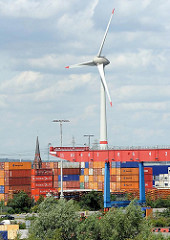 Containerlager und Portalkran auf dem Terminalgelände von Hamburg Altenwerder - im Hintergrund hinter den hoch gestapelten Metallboxen ragt der Kirchturm der ST. Gertrudkirche heraus, daneben eines der beiden Windkraftanlagen, die zu den höchsten Bau