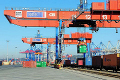 Portalkräne über den Gleisen auf dem Terminalgelände Burchardkai - ein Container wird auf den Güterwaggon abgesenkt.