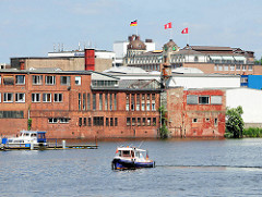 Altes Industriegebäude am Ufer der Bille in Hamburg Hammerbrook; im Hintergrund Fahnen auf dem Dach vom Störtebeker Haus.