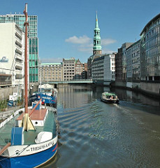 Schiffe auf dem Hamburger Nikolaifleet - ein Fahrgastschiff der Fleetrundfahrt fährt Richtung Trostbrücke - im Hintergrund der Kirchturm der St. Katharinenkirche.