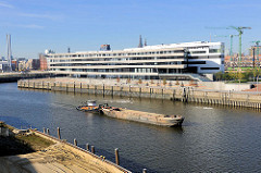Blick vom Petersenkai des Baakenhafens zum Versmannkai / Buenos Aires Kai - Neubau der Hafencity Universität; ein Schubschiff bringt eine Schute zur Baustelle im Hafenbecken.