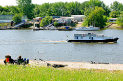 Angler am Ufer der Billwerder Bucht - ein Sportboot fährt Richtung Elbe.