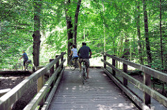 Holzbrücke mit Radfahrern über die Alster - Wald bei Wulksfelde, Gemeinde Tangstedt - Kreis Stormarn.