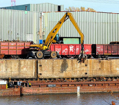 Die Ladung einer mit Schrott beladenen Schute wird mit einem Greifbagger gelöscht und in bereitstehende Güterwaggons verladen - Bilder aus dem Hamburger Stadtteil Waltershof.
