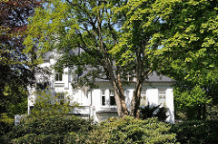 Villa hinter Bäumen und dichten Rhododendronbüschen in Hamburg Osdorf.