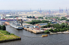 Blick auf Hamburg Steinwerder - ein Kriegsschiff liegt am Kai der Norderwerft im Reiherstieg - das Versorgungsschiff Berlin A 1411 liegt zur Reparatur im Hamburger Hafen. Auf der Norderelbe fährt eine gelbe Hafenfähre zum Anleger; im Hintergrund die