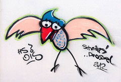 Schnapsdrossel - Vogel mit rotem Schnabel + ausgebreiteten Schwingen; Graffiti an einer Wand von einem Industriegebäude im Hamburger Hafen.