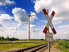 Bahnübergang und Andreaskreuz im Industriegebiet von Hamburg Altenwerder- lks. von der Windkraftanlage der Kirchturm der Kirche St. Gertrud.