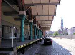 Rampe mit historischen Säulen am Zollamt Teerhof in der Hamburger Speicherstadt am Zollkanal - der Boden ist mit Pflastersteinen gepflastert - im Hintergrund der Zollzaun am Kanal und die Hamburger St. Katharinenkirche.
