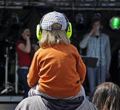 Musikveranstaltung auf dem Osterstrassenfest - verschiedene Band treten auf dem Strassenfest auf - Ein Kind sitzt auf den Schultern seinses Vaters und hat gegen den Lärm der Musik Ohrschützer auf.
