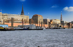 Blick in den Hamburger Binnenhafen im Winter - eisbedecktes Hafenwasser, Kontorhäuser an den Kajen, Kirchtürme, Blauer Himmel.
