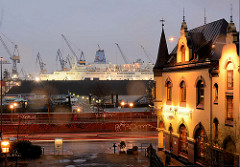Blick auf die Strasse St. Pauli Fischmarkt und zur Elbe, dem Hamburger Hafen - rechts ein Fischrestaurant mit beleuchteter Fassade - im Dock der Werft Blohm + Voss liegt eine Kreuzfahrtschiff.