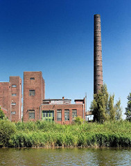 Gewerbliche Gebäude am Hoovekanal auf der Peute in Hamburg Veddel. Gebäude mit Klinkerfassade, hoher Schornstein; Gras am Ufer des Kanals in Hamburg Veddel.