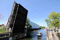 Geöffnete historische Holzhafenklappbrücke im Harburger Hafen. Ein Schiff verlässt den Holzhafen und fährt in den Lotsekanal ein.
