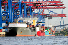 Containerfeeder im Hamburger Hafen am HHLA Containerterminal Burchardkai unter Containerbrücken - im Hintergrund die Köhlbrandbrücke.