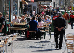 Restaurant mit Tischen in der Sonne auf der Strasse - Passanten auf dem Bürgersteig.