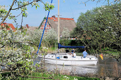 Segelboot auf der Este - blühende Obstbäume am Ufer, Fachwerkhäuser.