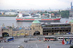 St. Pauli Landungsbrücken, einige Reisebusse stehen auf den Parkplätzen - ein Frachtschiff fährt elbabwärts.