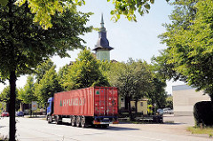 Containerlaster auf einer Strasse in Hamburg Wilhelmsburg - Giebelturm eines historischen Gasthauses am Wegesrand.