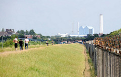 Klütjenfelder Hauptdeich am Spreehafen in Hamburg Wilhelmsburg (2010) - noch steht der mit Stacheldraht versehene Zollzaun. Spaziergänger in der Sonne am Ufer des Hamburger Spreehafens.