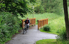Brücke über die Engelbek - Holzbrücke über den Bach in Hamburg Langenbek; Radfahrer auf dem Weg.