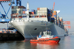 Schiffsbug der NYK HELIOS und roter Schlepper im Hamburger Hafen - Containerterminal Altenwerder. Das 2013 gebaute Containerschiff hat eine Länge von 365,50m und eine Breite von 48,40m; der Frachter kann 13208 TEU Container transportieren.