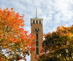 Kirchturm der Frohbotschaftskirche in Hamburg Dulsberg zwischen Herbstbäumen - Blätter herbstlich rot, braun und gelb gefärbt.