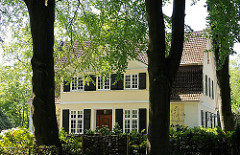 Alte hohe Bäume im Vorgarten einer Villa mit gelber Fassade in Hamburg Osdorf.