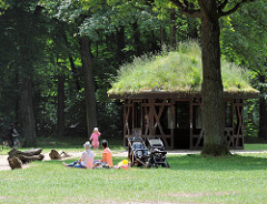 Spielplatz im Altonaer Volkspark von Hamburg Bahrenfeld - Mütter haben die Kinderkarren geparkt - Holzpavillon, das Dach ist mit Gras bewachsen.