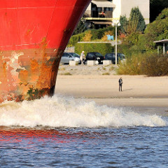 Schiffsbug in Fahrt - Gischt; Spaziergänger am Sandstrand in Hamburg Blankenese.