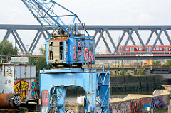 Hafenkran am Kai des Billehafens in Hamburg Rothenburgsort; S-Bahnzug auf der Brücke.